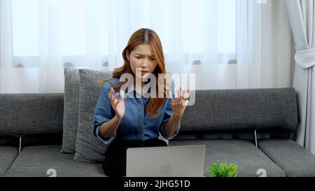 Eine verwirrte junge Frau, die mit Handgesten vor ihrem Laptop sitzt, um Dinge zu erklären Stockfoto