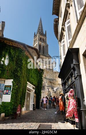 Die Kirche überragt die Touristen in einer engen, steilen Straße mit Kopfsteinpflaster in Saint Emilion, Frankreich, die von Geschäften gesäumt ist Stockfoto