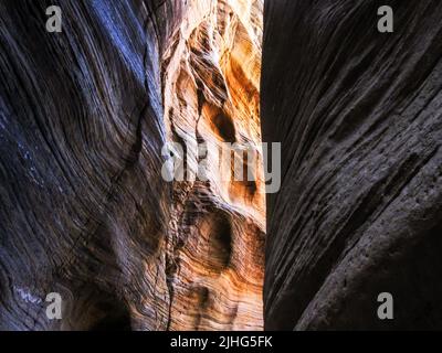 Blick auf die hohen Klippen eines engen Schlitzschluchtkanals bei Willis Creek, Utah, USA, mit Sonnenlicht, das bis zum Ende scheint Stockfoto