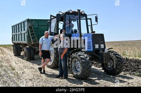 REGION SAPORISCHSCHSCHJA, UKRAINE - 17. JULI 2022 - während der Erntezeit stehen Männer neben einem Traktor in der Region Saporischschschja im Südosten der Ukraine. Dies Stockfoto