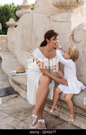 Kleinkind Mädchen Anwendung Lipgloss auf Mutterlippen auf Stein Bank Puente Del Mar Brücke in Valencia Stockfoto