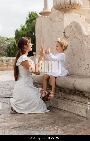 Lächelndes Kleinkind spielt mit Mama auf der Steinbank der Puente Del Mar Brücke in Valencia Patty Cake Spiel Stockfoto