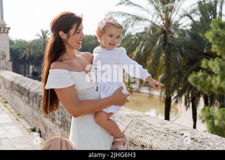 Positive Mutter blickt auf eine kleine Tochter, die mit dem Finger auf die Brücke Puente Del Mar in Valencia zeigt Stockfoto