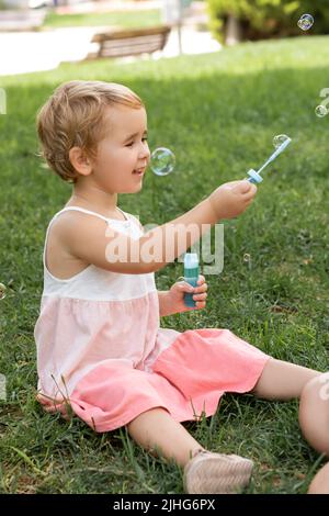 Fröhliches Kind im Sommerkleid, das im Park mit Seifenblasen spielt Stockfoto