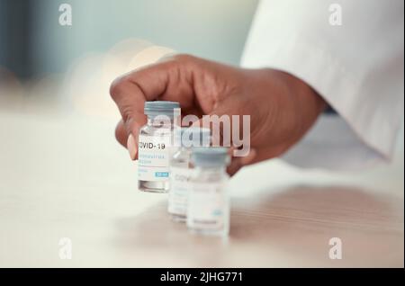 Nahaufnahme eines Arztes, der Flaschen mit Covid-Impfstoff auf einen Tisch legte. Hände eines Arztes, der ein Gegengift des Corona-Virus hält. Putting von medizinischem Fachpersonal Stockfoto