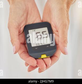 Nahaufnahme einer älteren diabetischen Frau, die ihren Blutzuckerspiegel mit einem Diabetes-Lesegerät überprüft. Eine unbekannte ältere Frau, die eine Stockfoto