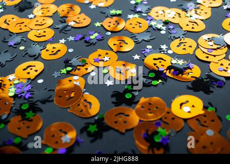 Halloween Hintergrund: Glänzendes Konfetti in Form von orangefarbenen Kürbissen, schwarzen Spinnen und bunten Sternen grün, lila Farbe. Stockfoto