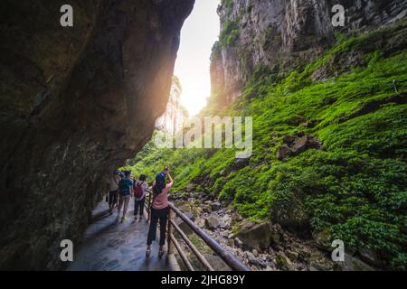 Wulong, China - August 2019 : Touristen, die Fotos von einer atemberaubenden Landschaft machen, während sie auf einem schmalen Pfad in einer Schlucht inmitten der Karstlandschaft der Wul spazieren Stockfoto