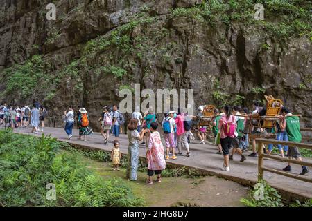 Wulong, China - August 2019 : Touristen trugen in einem Abfall auf dem schmalen Bergwanderweg in der Schlucht Tal zwischen Karst Kalkstein Felsen formati Stockfoto