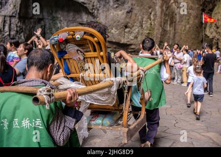 Wulong, China - August 2019 : Touristen trugen in einem Abfall auf dem schmalen Bergwanderweg in der Schlucht Tal zwischen Karst Kalkstein Felsen formati Stockfoto