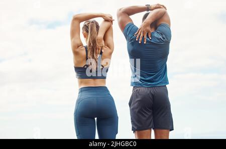 Junge Männer und Frauen vom Rücken aus fit halten und Arme und Trizeps strecken, indem sie den Ellbogen mit den Händen hinter dem Kopf zur Wirbelsäule ziehen, während sie im Freien trainieren. Zwei Stockfoto