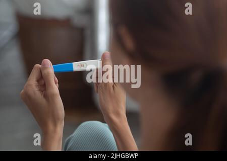 Glück junge Frau unter Schwangerschaftstest, während aufgeregt und zufrieden im Schlafzimmer zu Hause, glückliche Mutter mit Lächeln und Ausdruck mit Liebe, ovul Stockfoto