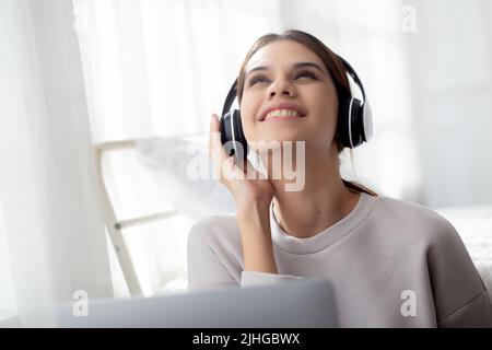 Glückliche junge Frau trägt Kopfhörer Musik hören, während mit Laptop-Computer und singen mit Spaß und genießen Sie im Wohnzimmer, Glück weiblich w Stockfoto