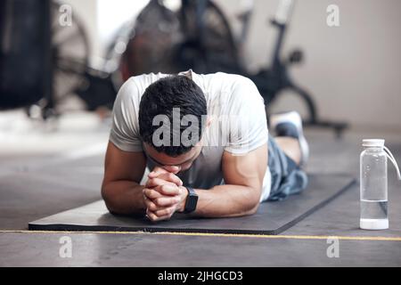 Ein erschöpfter junger hispanischer Mann, der eine Pause einnahm, während er in einem Fitnessstudio kämpfte, um Sport zu treiben. Muskulöser gemischter Rennmensch, der müde, enttäuscht und bereit aussieht Stockfoto