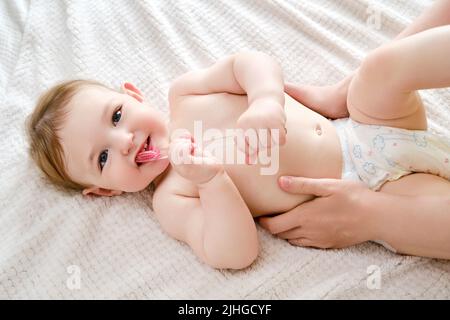 Eine Mutter lehrt ein glückliches Kleinkind Baby, seine Zähne auf einem Heimbett zu putzen. Kind im Alter von einem Jahr Stockfoto