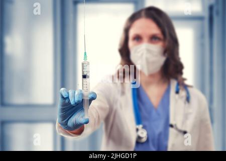 Ärztin mit Insulinspritzen in der Hand auf einem Klinikhintergrund, Platz für Text kopieren. Eine Krankenschwester in einer medizinischen Maske bereitet sich auf eine Injektion vor, conce Stockfoto