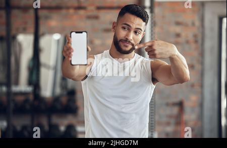 Sportler, der einen Gesichtsausdruck mit seinem Telefon macht. Fit junger Mann zeigt seinen mobilen Bildschirm im Fitnessstudio. Hübscher junger Mann mit seinem Stockfoto