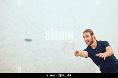 Athletischer junger Squashspieler, der während eines Spiels auf dem Platz mit Copyspace den Ball trifft. Fit aktiven kaukasischen männlichen Athleten Training und spielen in einem Stockfoto