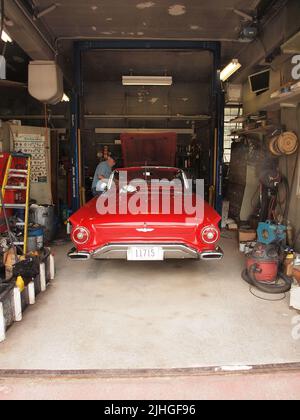 Ein klassischer roter Ford Thunderbird aus dem Jahr 1957, der in einer traditionellen Tankstelle in Pennsylvania zu sehen ist. Der Besitzer kann gesehen werden, wie er am Auto arbeitet. Stockfoto