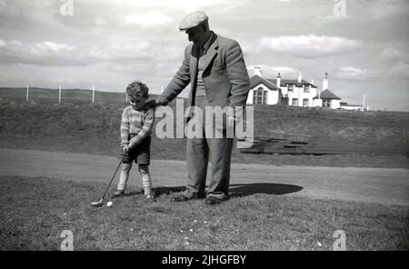 1950s, historischer, schottischer Golfprofi und Golfclubmacher, Tom Reekie mit seinem jungen Enkel, auch Tom genannt, außerhalb des Elie Golf Club, Fife, Schottland, Großbritannien. Geboren 1880 in St.Monans, nahm Tom 1895 eine Lehre und arbeitete bei dem Golfclub-Hersteller George Forrester in Earlsferry, wo er bis zu seiner Dienstzeit WW1 arbeitete. Nachdem er den Krieg überlebt hatte, gründete er 1919 sein eigenes Geschäft als Golfprofi und Clubmacher in Elie und 1946 wurde es Tom Reekie & Son, als sein Sohn John zu ihm kam. Stockfoto