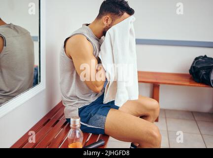 Junger Spieler, der sein Gesicht mit einem Handtuch abwischt. Müder Mann, der nach einem Squash-Match sein Gesicht mit einem Handtuch putzte. Squatch-Spieler sitzt in seinem Turnschrank Stockfoto