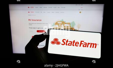 Person mit Mobiltelefon und Logo der US State Farm Mutual Automobile Insurance Company auf dem Bildschirm vor der Webseite. Konzentrieren Sie sich auf die Telefonanzeige. Stockfoto