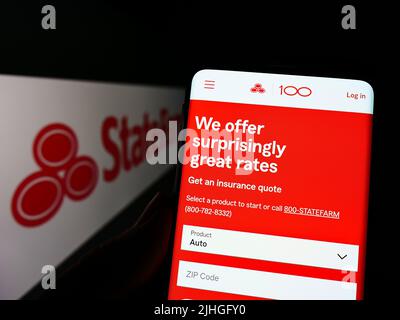 Person, die Mobiltelefon mit Website der State Farm Mutual Automobile Insurance Company auf dem Bildschirm mit Logo hält. Konzentrieren Sie sich auf die Mitte des Telefondisplays. Stockfoto