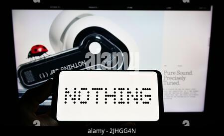 Person, die ein Mobiltelefon mit dem Logo der britischen Firma Nothing Technologies Limited auf dem Bildschirm vor der Webseite hält. Konzentrieren Sie sich auf die Telefonanzeige. Stockfoto