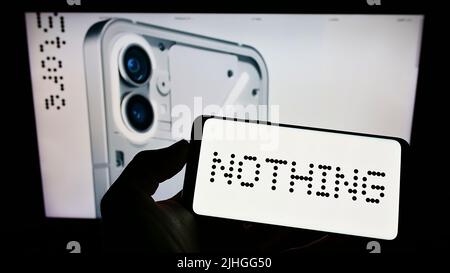 Person, die Mobiltelefon mit dem Logo der britischen Firma Nothing Technologies Limited auf dem Bildschirm vor der Business-Webseite hält. Konzentrieren Sie sich auf die Telefonanzeige. Stockfoto