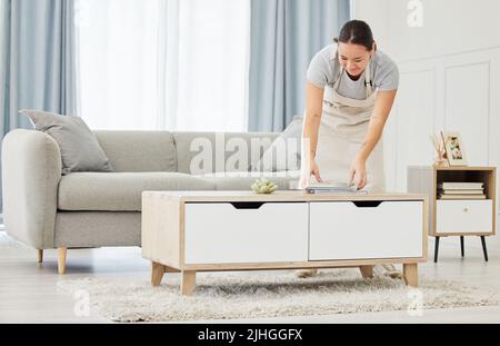 Eine schöne lächelnde junge Frau mit gemischter Rasse, die die Oberflächen ihres Hauses putzt. Glückliche asiatische Hausangestellte Verpackung Bücher in einen ordentlichen Haufen auf die Stockfoto