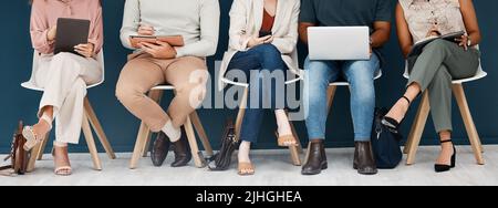 Eine Gruppe von Geschäftsleuten, die in einem Büro in einer Reihe auf Stühlen sitzen. Fünf Geschäftsleute, die in einem Wartezimmer mit Technologie sitzen Stockfoto