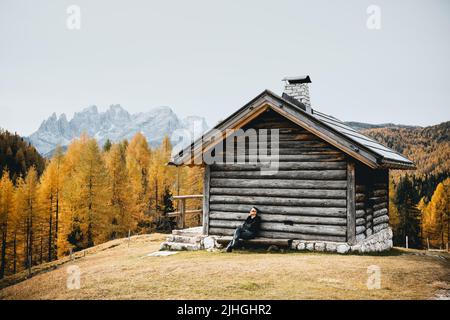 Unglaublicher Herbstblick im Valfreda-Tal in den italienischen Dolomiten. Holzhütte, gelbes Gras, orangefarbener Lärchenwald und schneebedeckte Berggipfel im Hintergrund. Dolomiten, Italien. Landschaftsfotografie Stockfoto