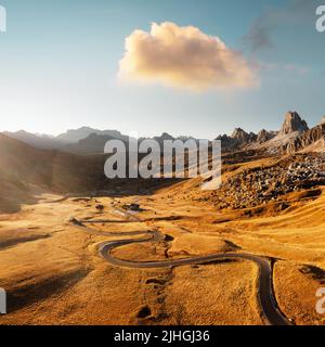 Malerische Luftaufnahme auf kurvenreicher Straße im herbstlichen Bergtal bei Sonnenuntergang. Das goldene Abendlicht beleuchtet die Berge und das orangefarbene Gras. Giau-Pass, Dolomiten, Dolomiten, Italien Stockfoto