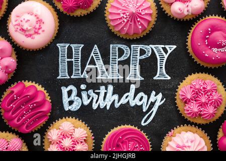 Overhead-Ansicht von rosa Geburtstagskuchen auf einer Kreidetafel mit Happy Birthday Gruß in Kreide angeordnet Stockfoto