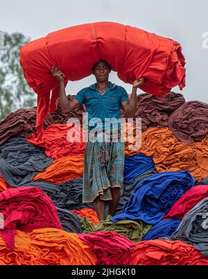 Bunte Decken werden von Arbeitern auf LKWs geladen. Textilindustrie in Bangladesch Stockfoto