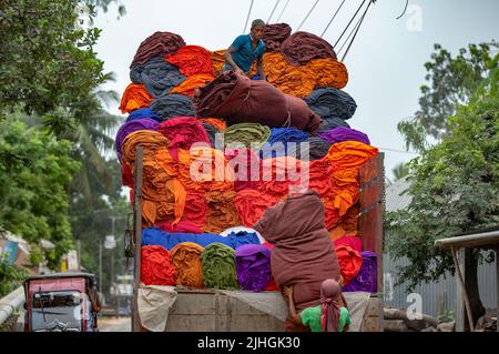 Bunte Decken werden von Arbeitern auf LKWs geladen. Textilindustrie in Bangladesch Stockfoto