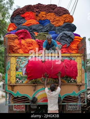 Bunte Decken werden von Arbeitern auf LKWs geladen. Textilindustrie in Bangladesch Stockfoto