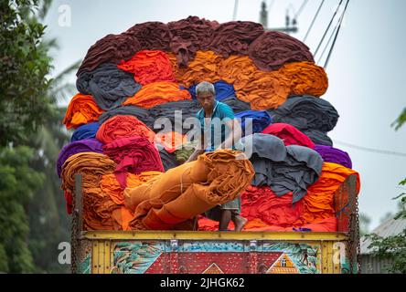 Bunte Decken werden von Arbeitern auf LKWs geladen. Textilindustrie in Bangladesch Stockfoto