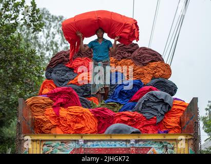 Bunte Decken werden von Arbeitern auf LKWs geladen. Textilindustrie in Bangladesch Stockfoto