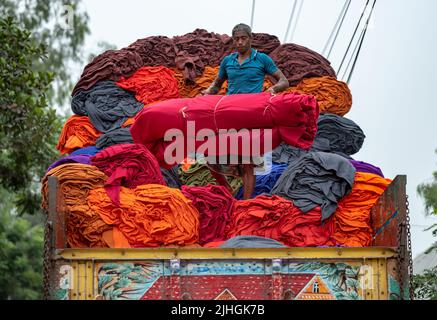 Bunte Decken werden von Arbeitern auf LKWs geladen. Textilindustrie in Bangladesch Stockfoto