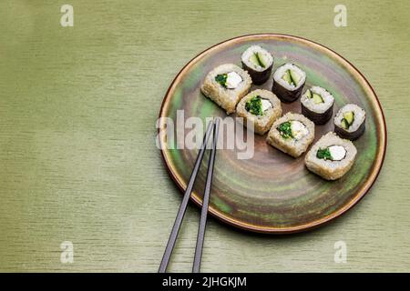 Sushi-Brötchen und Essstäbchen auf grünem Teller. Sojasauce in Schüsseln. Speicherplatz kopieren. Draufsicht. Grüner Hintergrund Stockfoto