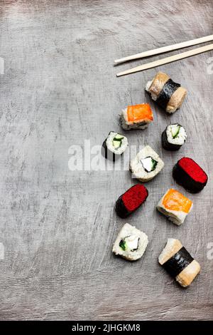 Verschiedene Arten von Sushi und Essstäbchen auf dunkelbraunem Hintergrund. Speicherplatz kopieren. Flach liegend Stockfoto