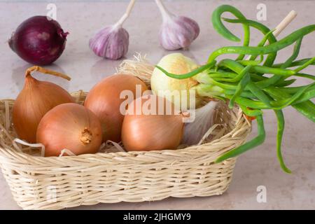 Grüne Zwiebeln, Knoblauch und rote Zwiebeln in einem Weidenkorb Stockfoto