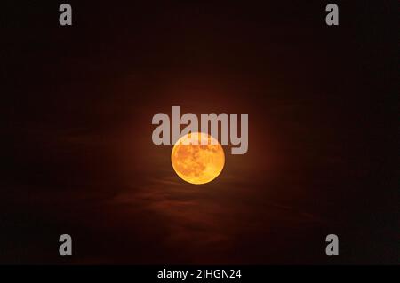 Der April Pink Supermond leuchtet stark und beleuchtet einige Wolken am Nachthimmel. Stockfoto