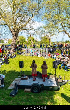Zwei Sängerinnen auf einer kleinen Bühne singen bei strahlendem Sonnenschein bei einem Event in Sandwich in den 40er Jahren vor einem hauptsächlich sitzenden Publikum Vintage-Songs. Stockfoto