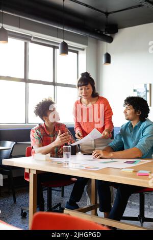 Kreative, multirassische Kolleginnen und Kollegen diskutieren über das Diagramm am Tisch im Büro Stockfoto