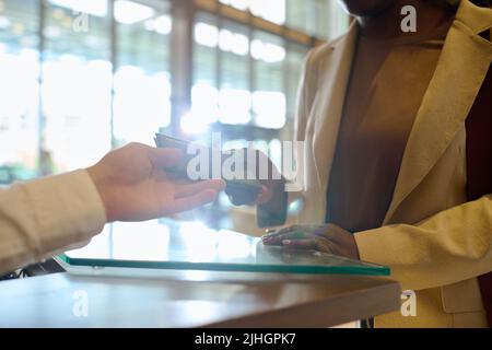 Hand eines jungen Mannes an der Rezeption, der den Pass einer weiblichen Person nimmt, die am Schalter in der geräumigen Lounge des modernen Hotels steht Stockfoto