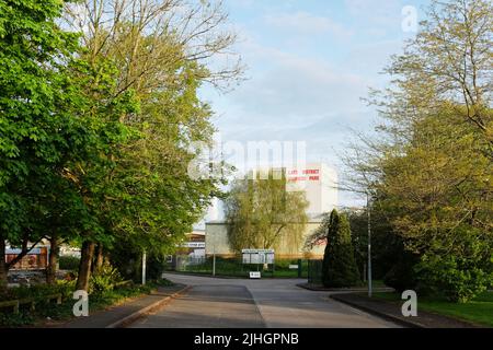 Von Bäumen gesäumte Straße in Richtung eines großen Gebäudes in einem Industriepark mit Schild zum Lake District Business Park in Kendal, Cumbria. Stockfoto