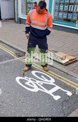 Bild eines Straßenarbeiters, der auf einem weißen Radweg-Schild mit einem gasbetriebenen Brenner brennt, um einen Radweg anzuzeigen. Stockfoto