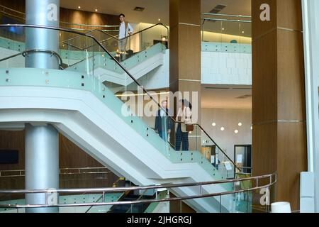 Zwei junge multikulturelle Kollegen in formeller Kleidung, die während einer Geschäftsreise auf der Treppe in der Hotellounge ein Gespräch führen Stockfoto